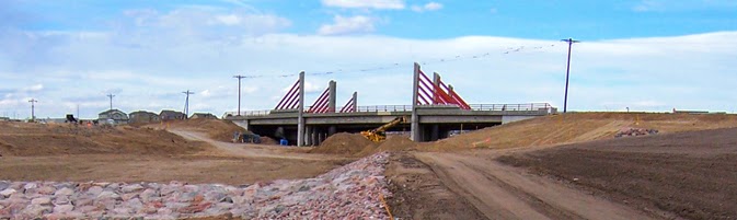 Bridge under construction with red support beams and dirt roads leading up to it